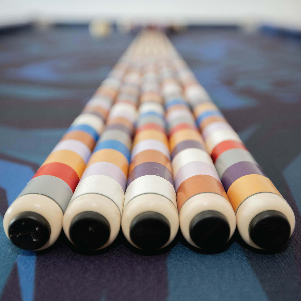 Five hand-painted pool cues lined up on the table