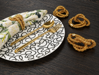 Black and white Squiggly plate with gold napkin rings and Cream Floral Garden napkin on black wood