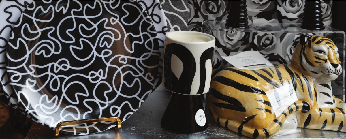 Black and white squiggly melamine plate, black and white candle and a ceramic tiger on a table